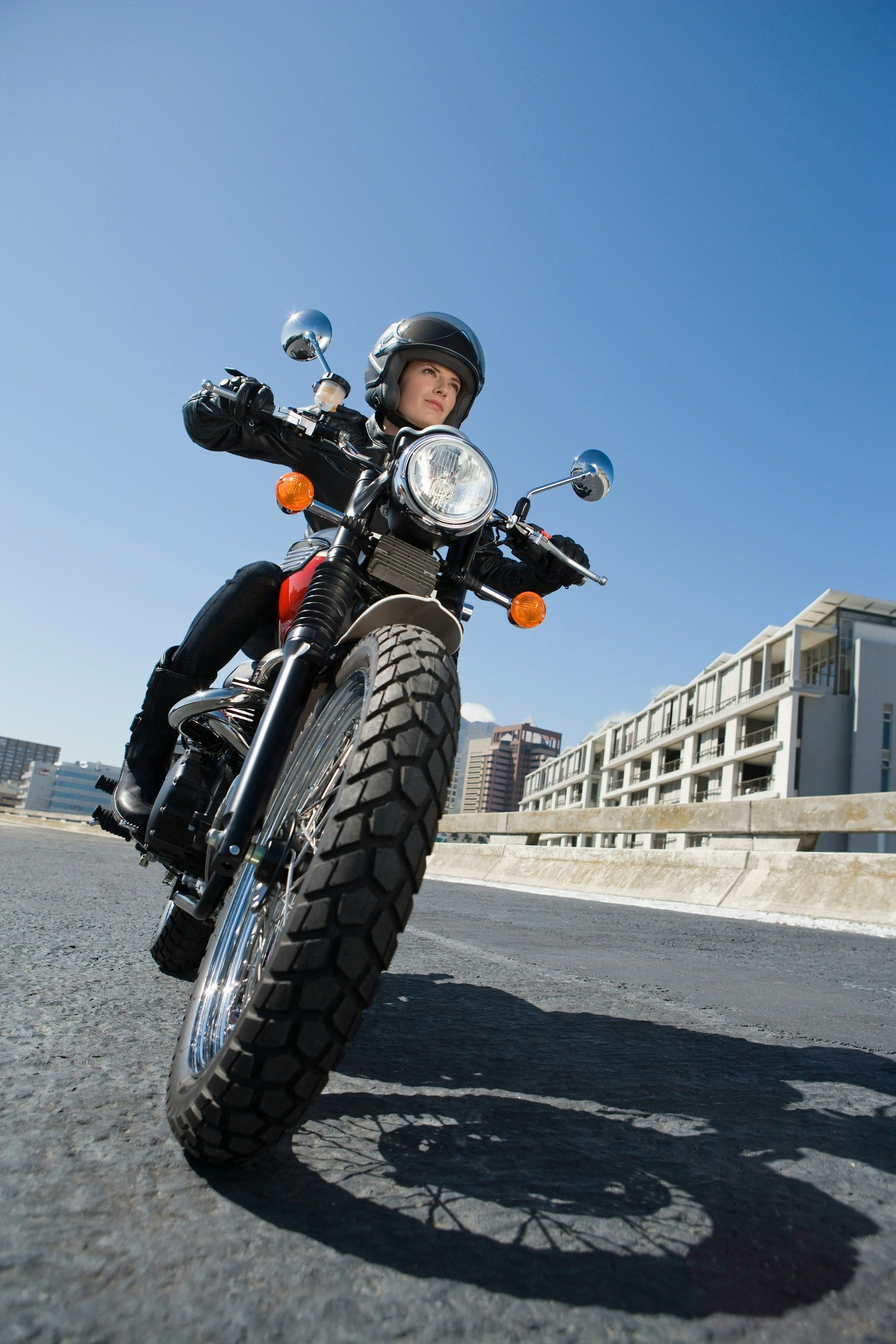 Motorcyclist riding a black bike on a road, shot from a low angle under a clear blue sky.
