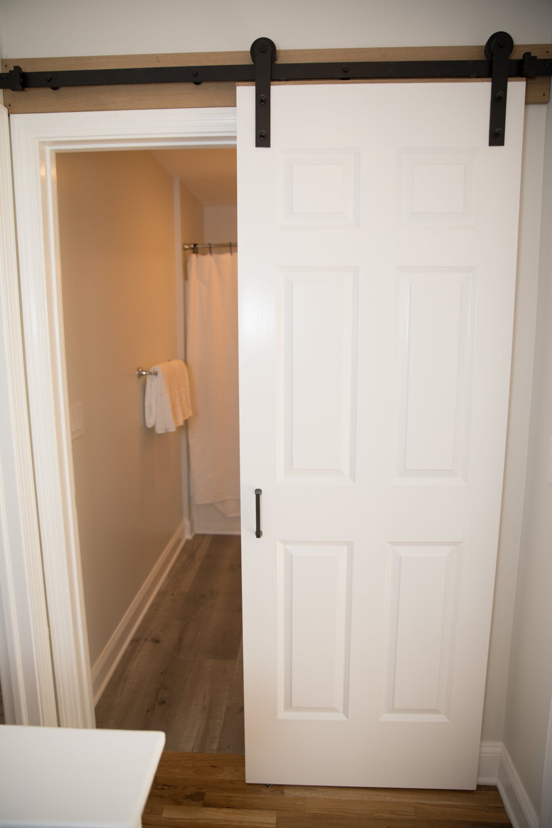 White barn door partially covering a doorway to a bathroom with a shower and towel rack.