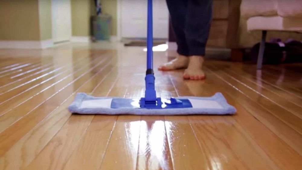 Person mopping a shiny, wooden floor with a blue mop, indoors.
