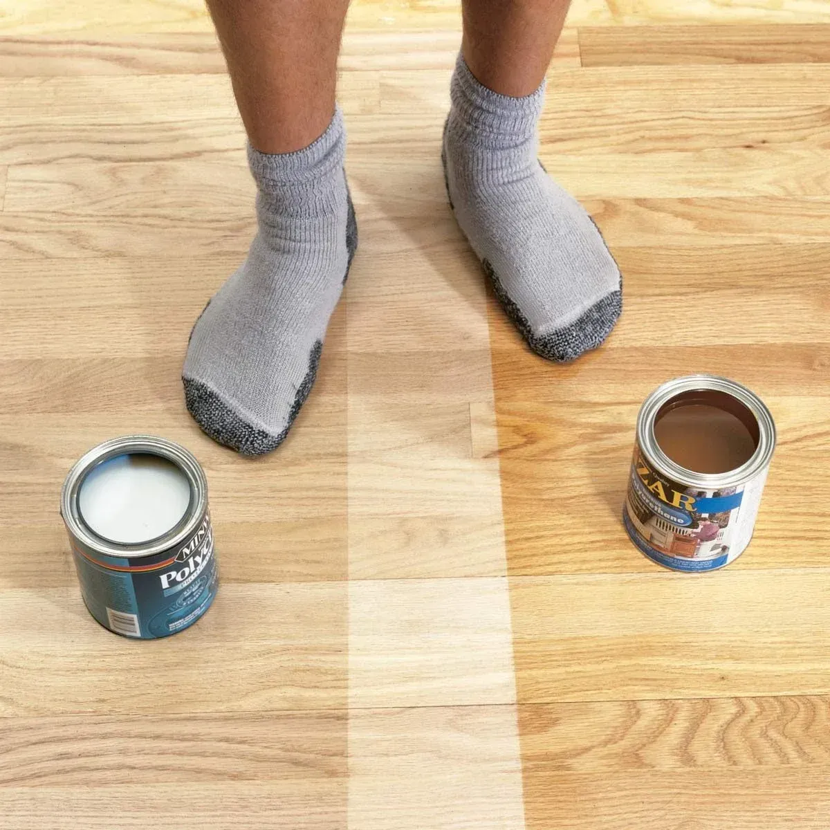 Person in socks stands on a wood floor, half treated with clear finish, with paint cans on each side.