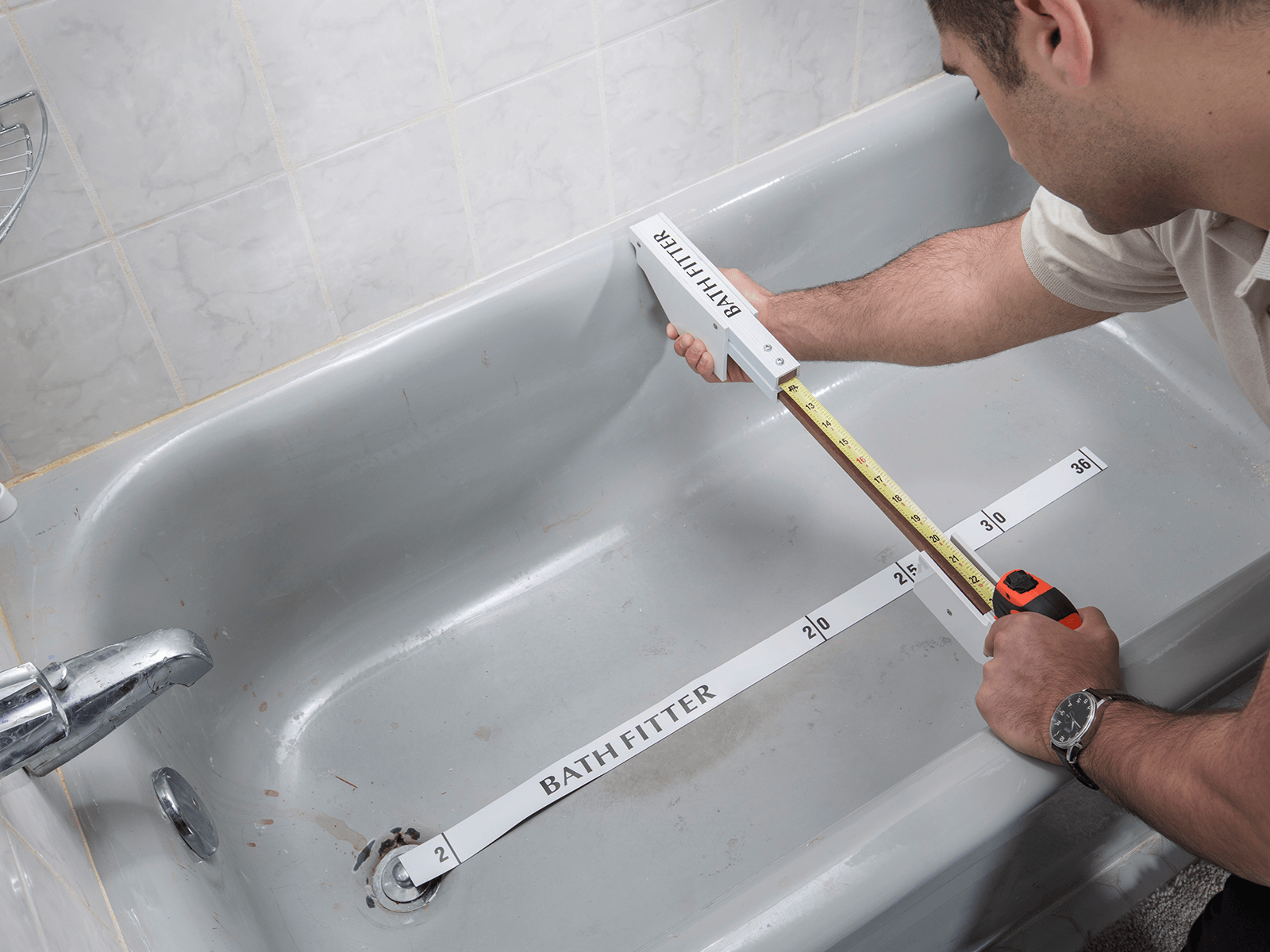 Person measuring the inside of a bathtub with a tape measure tool in a bathroom.