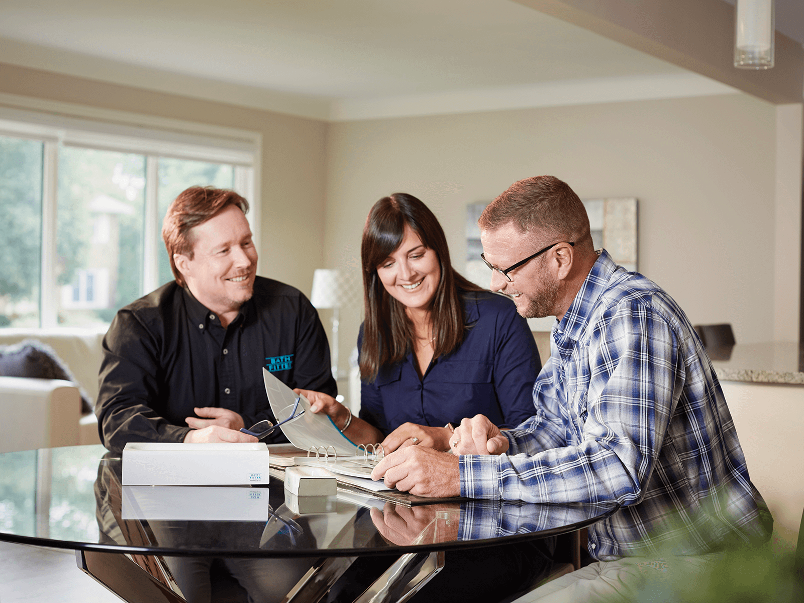Three people reviewing documents at a table. Woman in blue shirt pointing at papers. Two men look on.