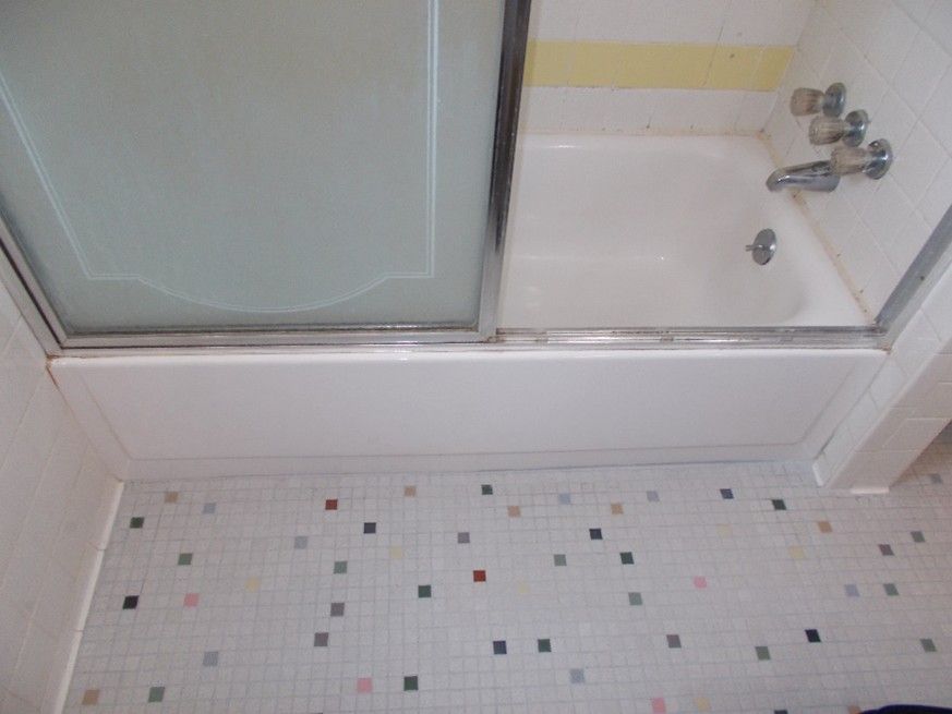 Bathroom with white tub, sliding glass shower doors, and tiled floor with colored squares.