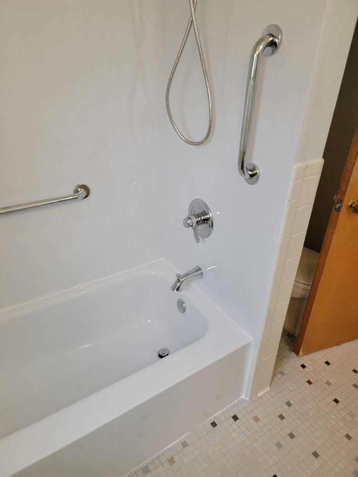 White bathtub with grab bars; shower fixtures; door visible in background.