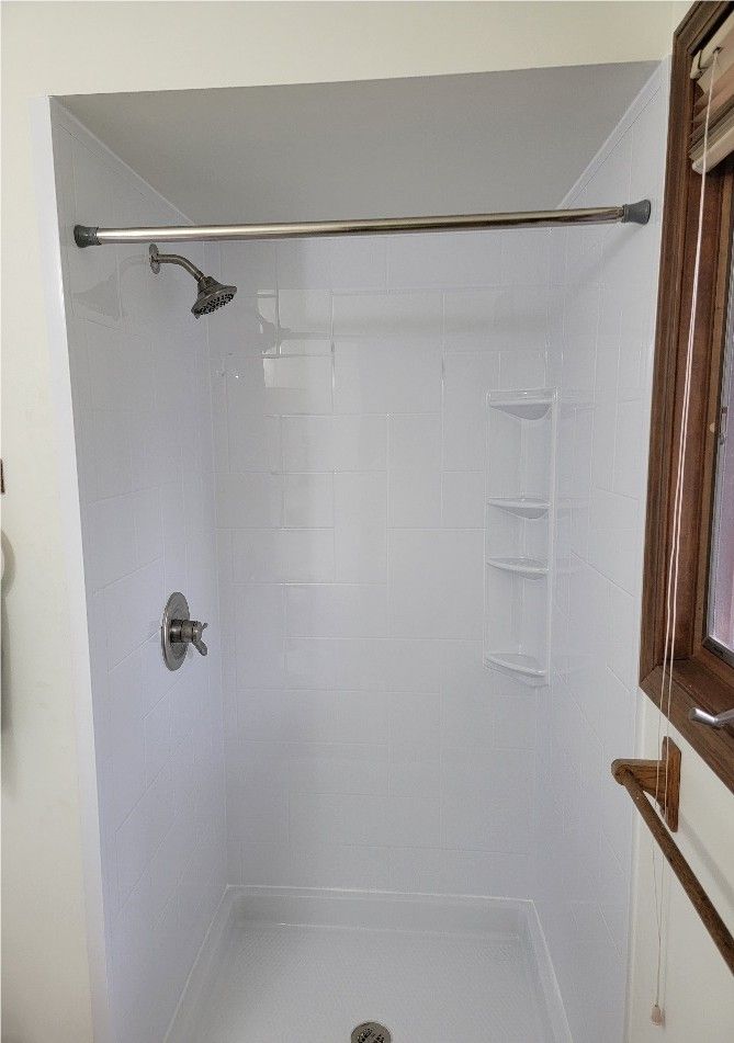 White-walled shower stall with shower head, faucet, shelves, and a shower rod.