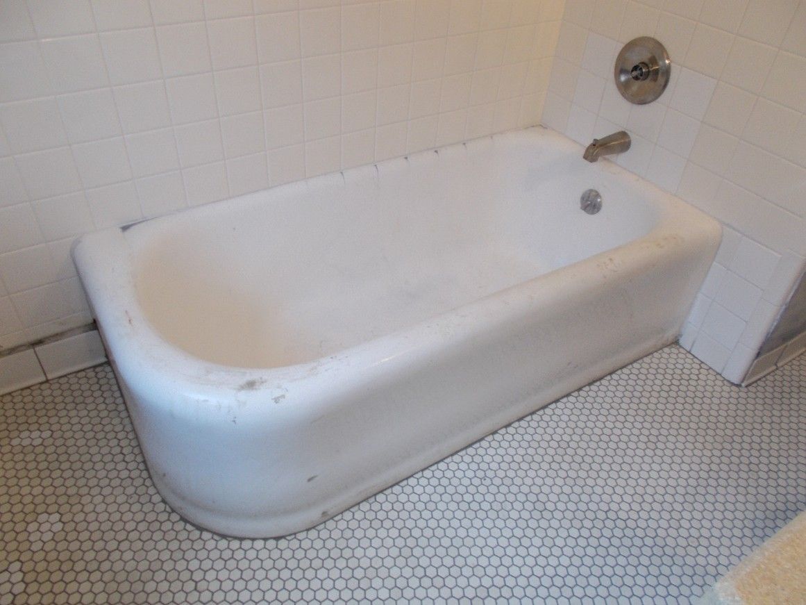 White bathtub against white tiled wall and floor. Faucet and showerhead on the wall.