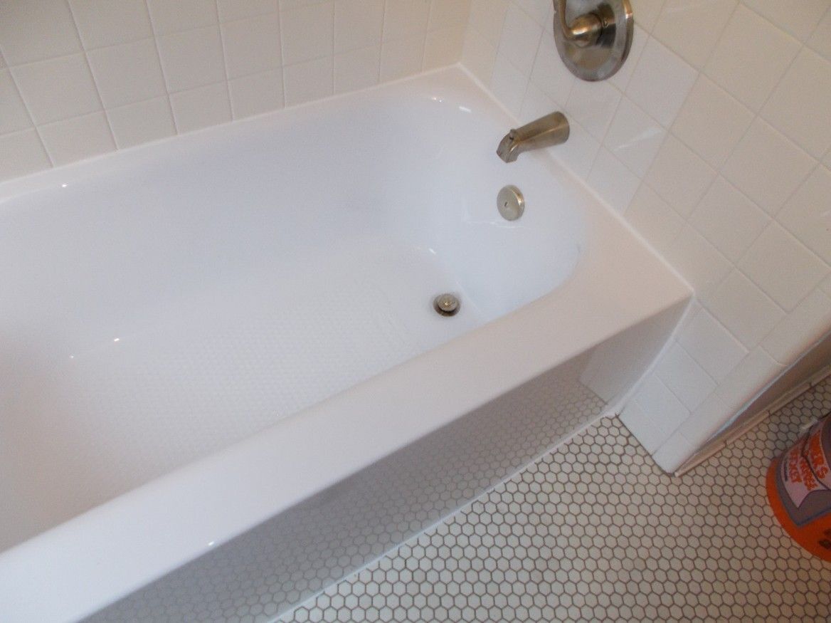 White bathtub with faucet and drain, next to tiled wall and floor.