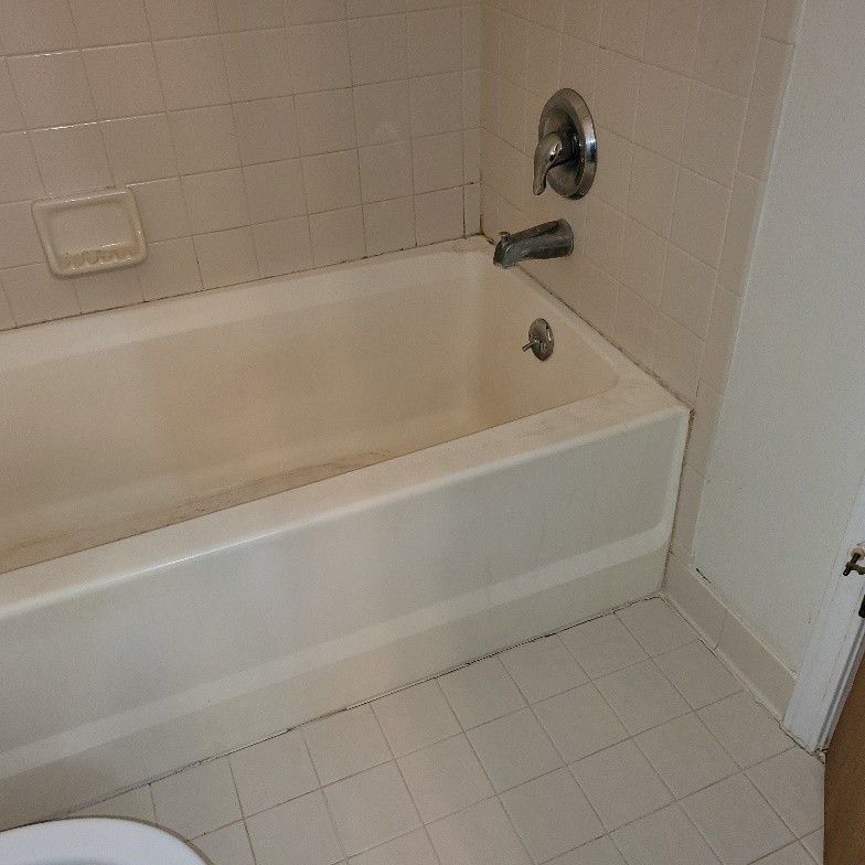 Bathtub with shower fixtures in a bathroom, white tiles, soap dish.
