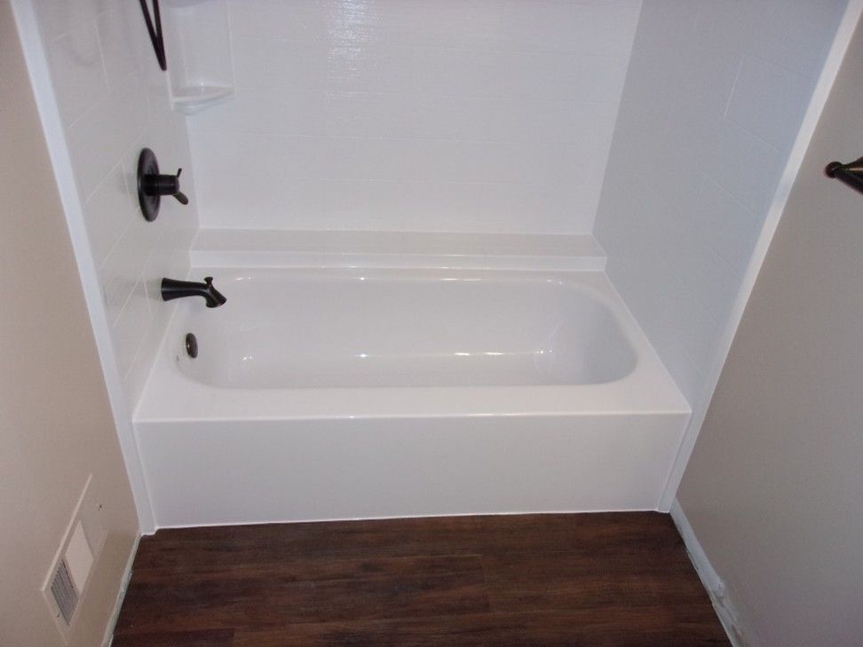 White bathtub with black fixtures in a small bathroom with dark wood-look flooring and white walls.