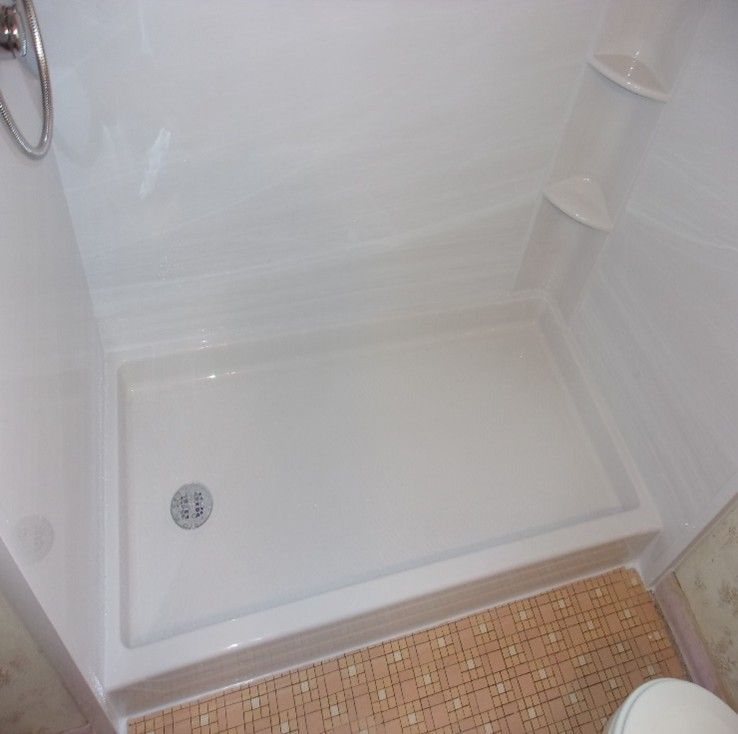 White, rectangular shower with a built-in seat and showerhead; brown and pink tiled floor.
