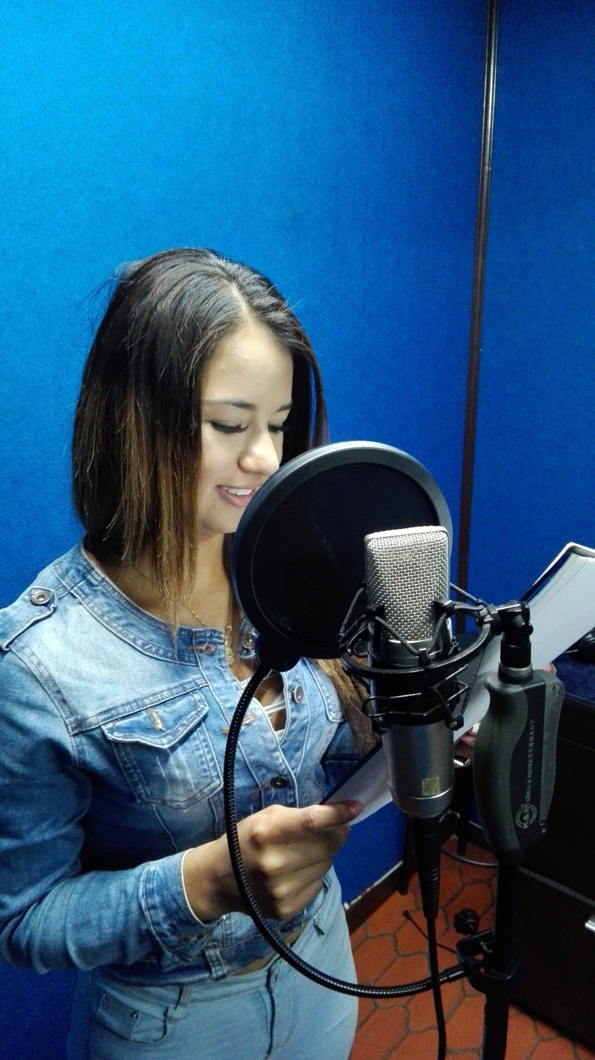 Mujer con chaqueta vaquera grabando voces en un micrófono en un estudio.