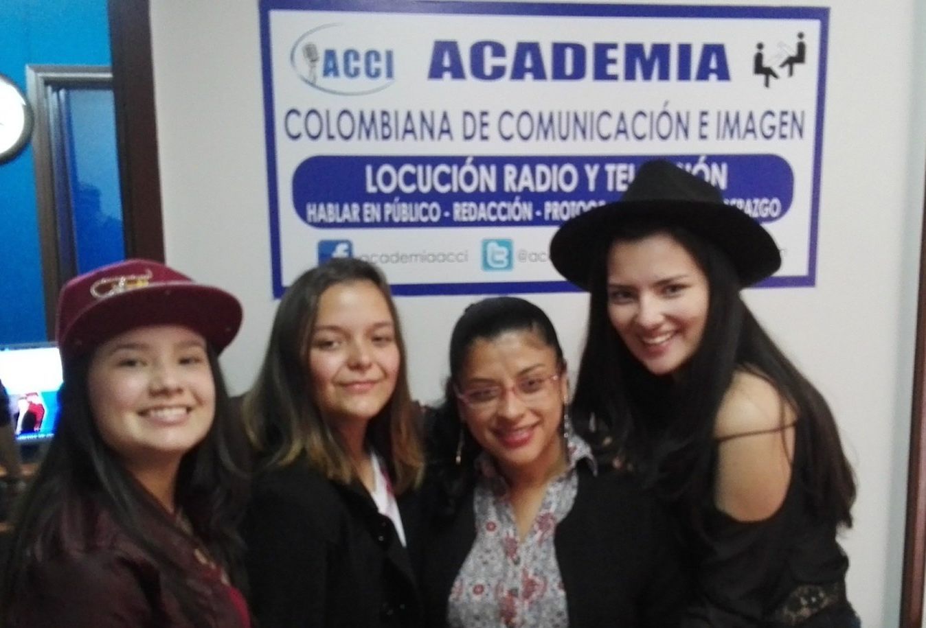 Personas grabando audio en una cabina de sonido; dos mujeres sosteniendo papeles junto a micrófonos, un hombre y otra persona observando.