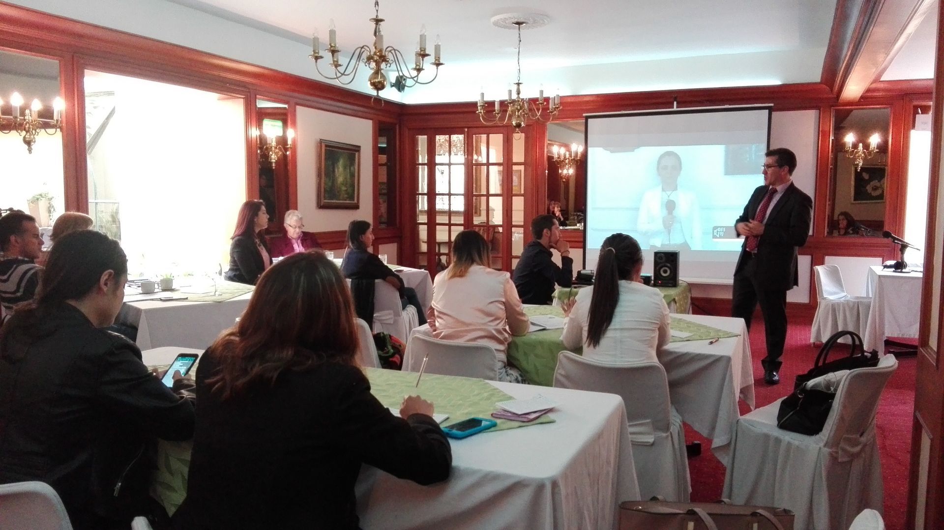 Un hombre presenta en una reunión de negocios. Los asistentes están sentados a una mesa con comida.