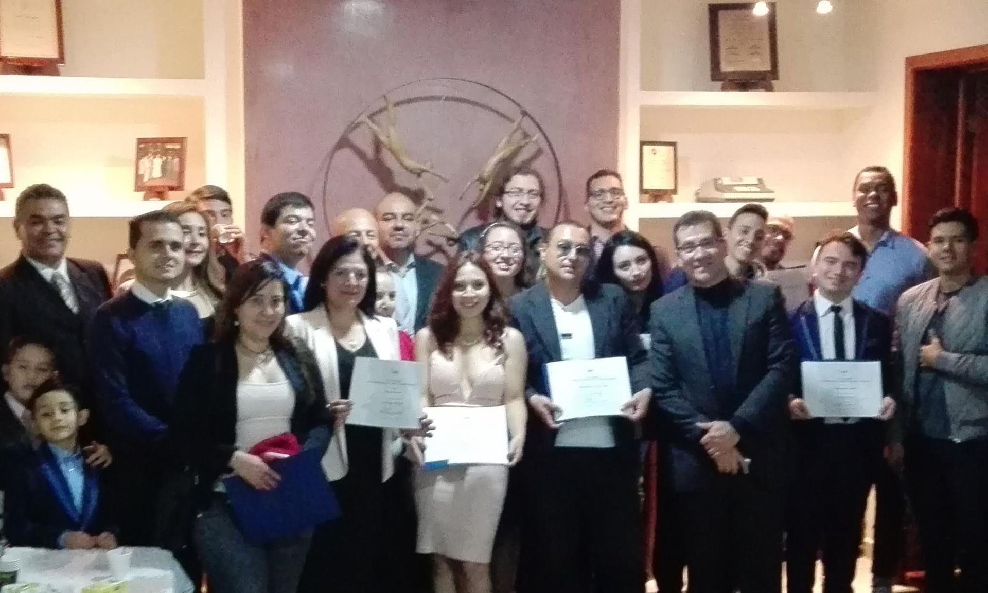 Aula con estudiantes con camisetas verde azulado escuchando a un presentador, diagramas en pantallas.
