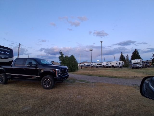 Black truck parked near RVs on a grassy field at dusk, with a cloudy blue sky.