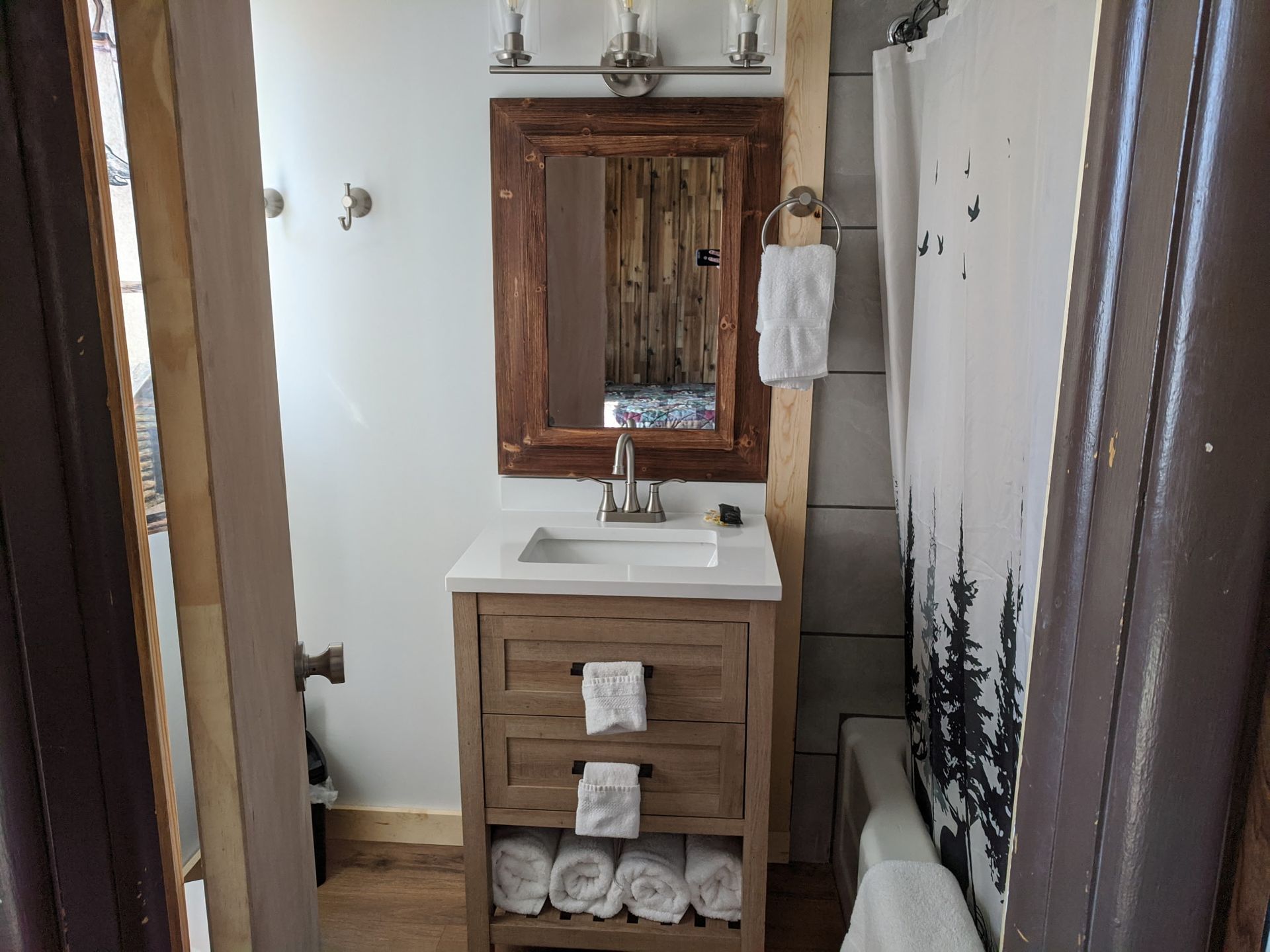 Rustic bathroom with wooden vanity, mirror, shower curtain, and white towels.
