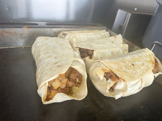 Burritos being grilled on a flat top. Filling is visible.