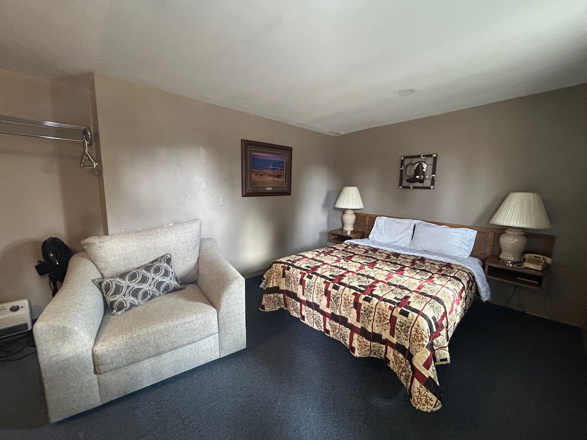 A hotel room with a bed , chair , lamps and a picture on the wall.
