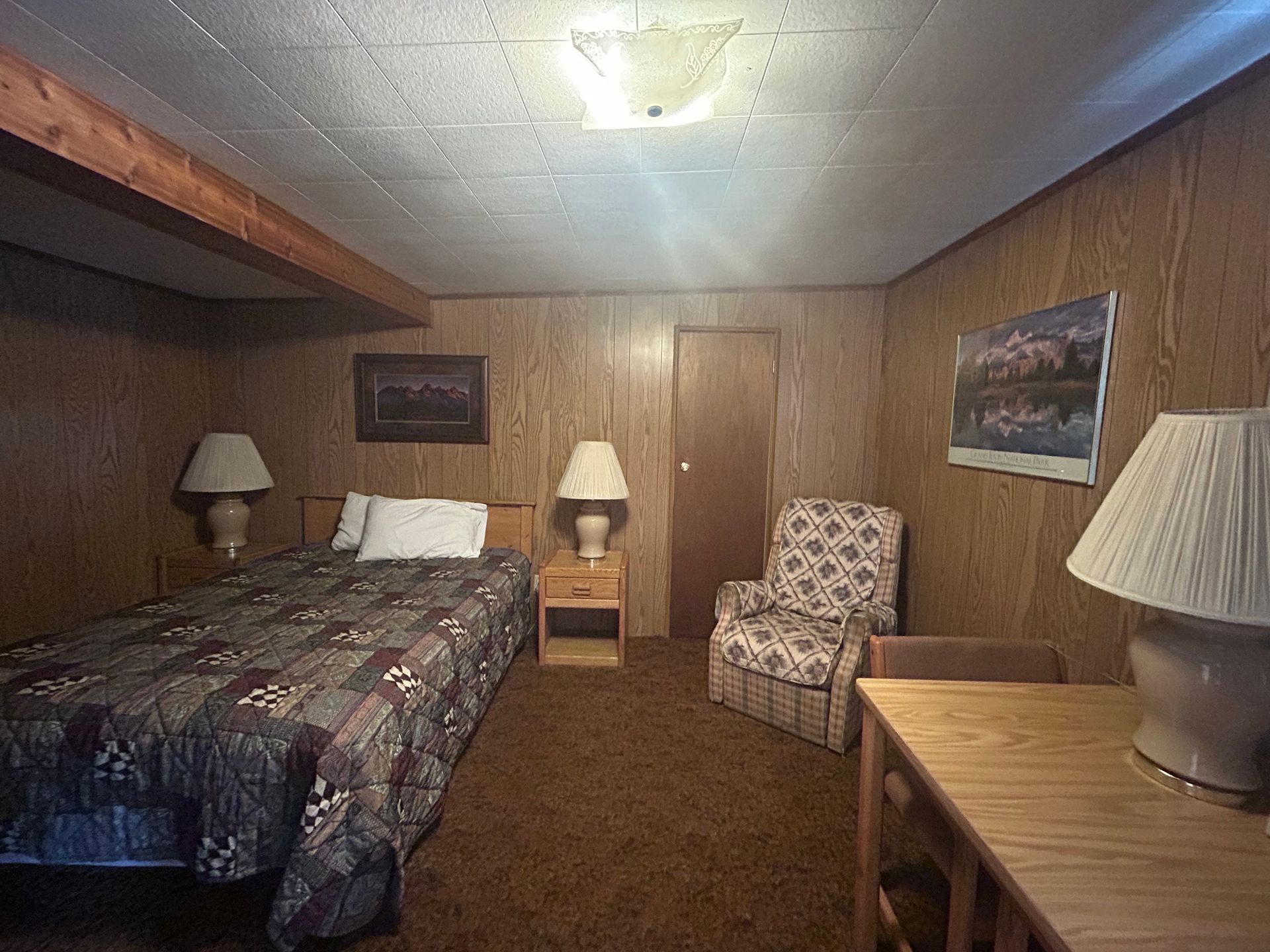 A bedroom with a bed , chair , table and lamps.