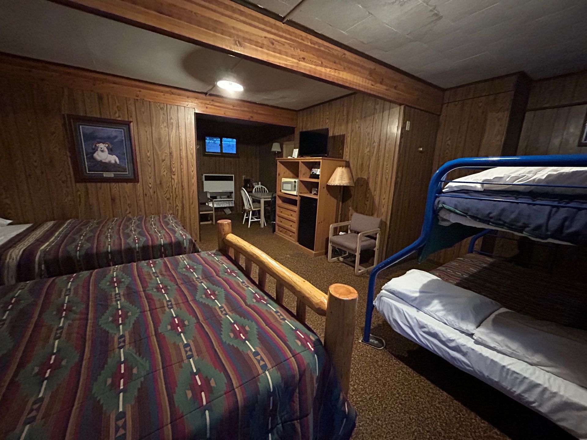 Bedroom with two beds, bunk beds, wood paneling, and a small desk area.