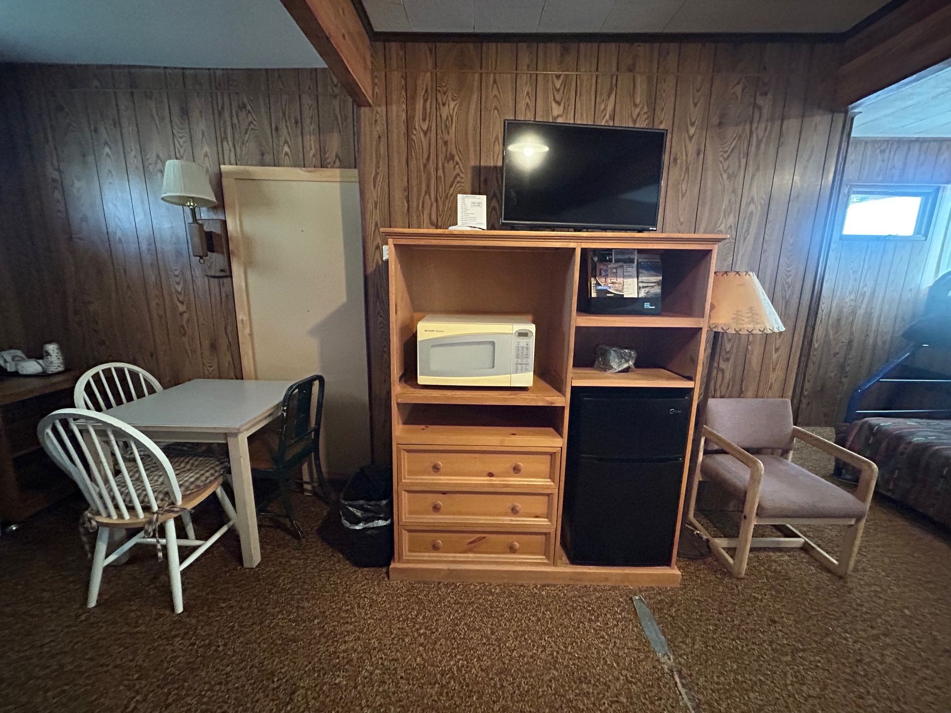 A small motel room with a table and chairs, a cabinet with a microwave, mini-fridge, and TV.