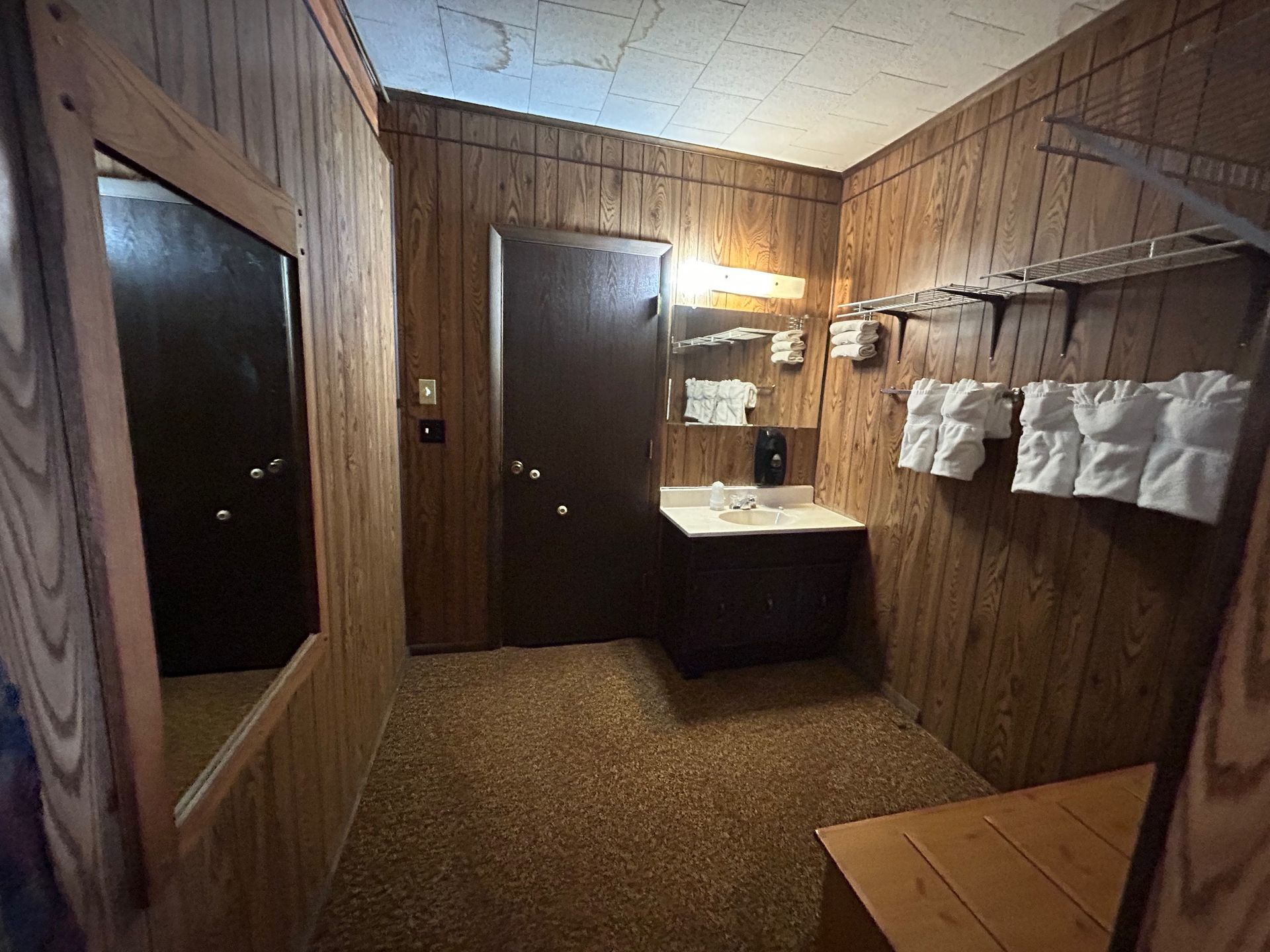 A small bathroom with brown wood paneling, a mirror, sink, and towels.