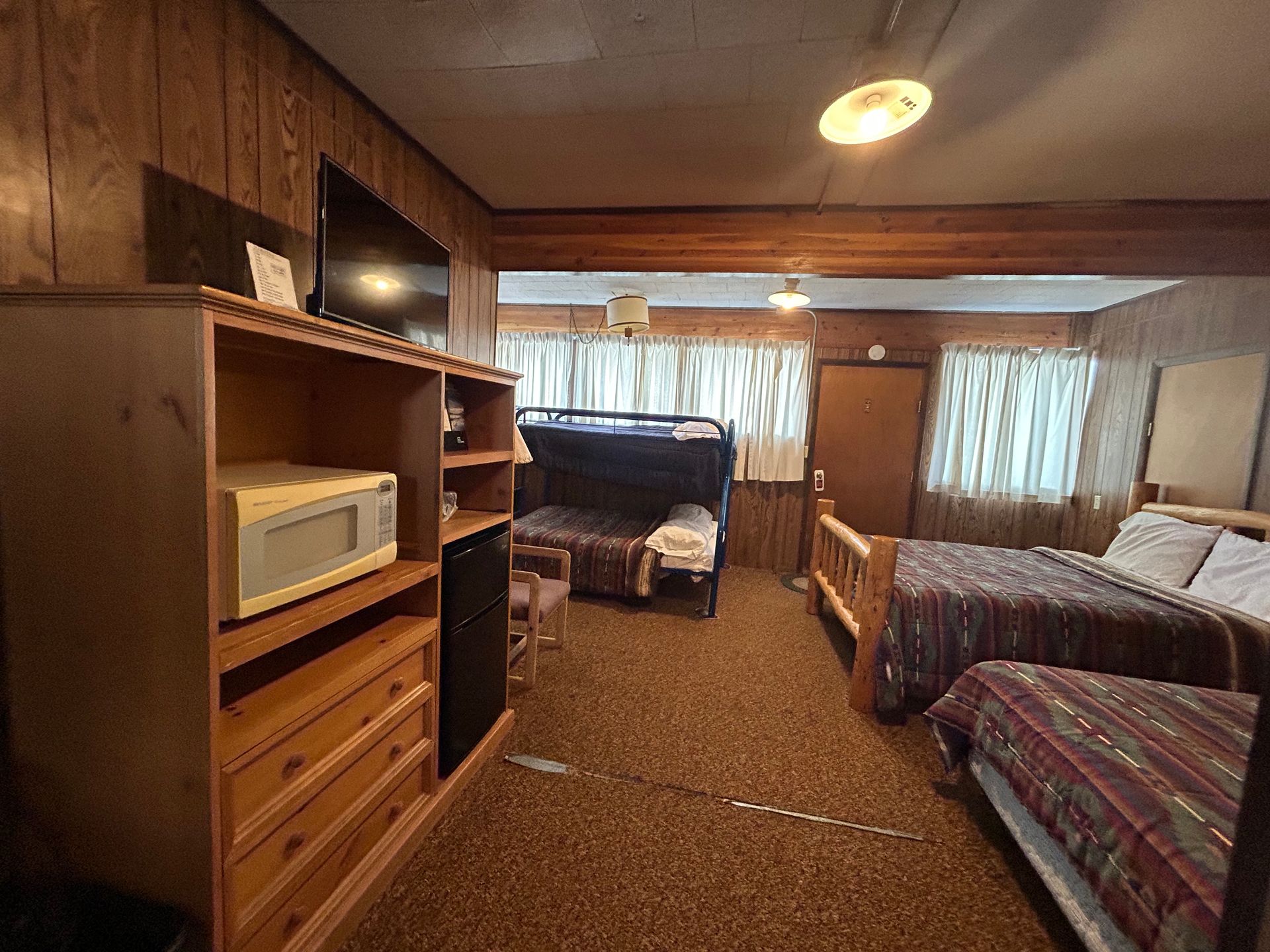 A hotel room with two beds, a bunk bed, and a wooden cabinet with a microwave.