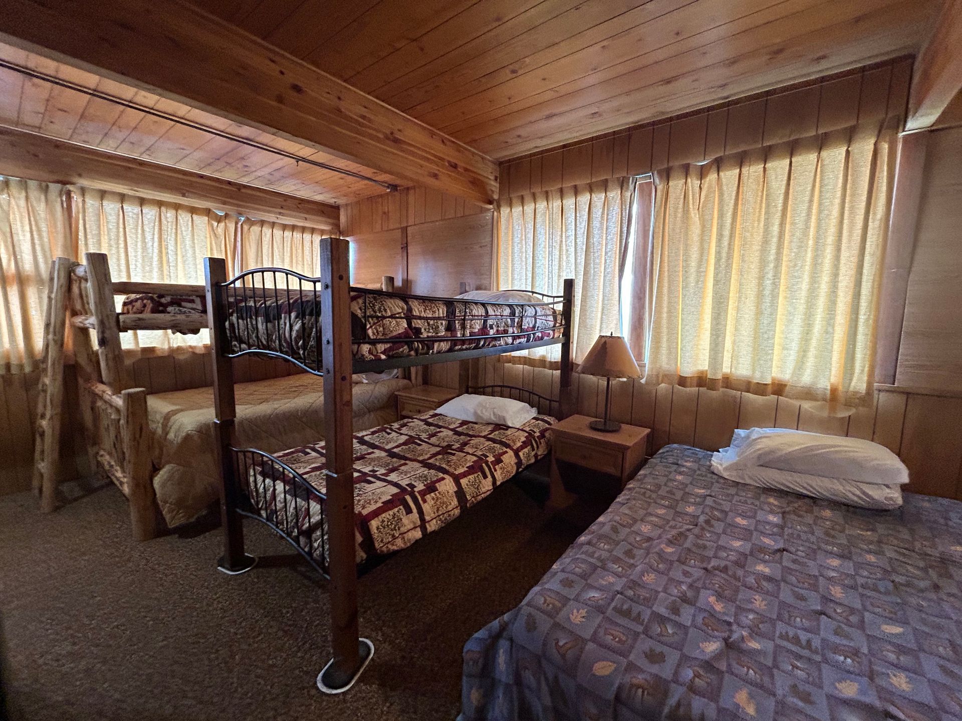 Bedroom with wood paneling, bunk beds, and a single bed, all with patterned bedding.