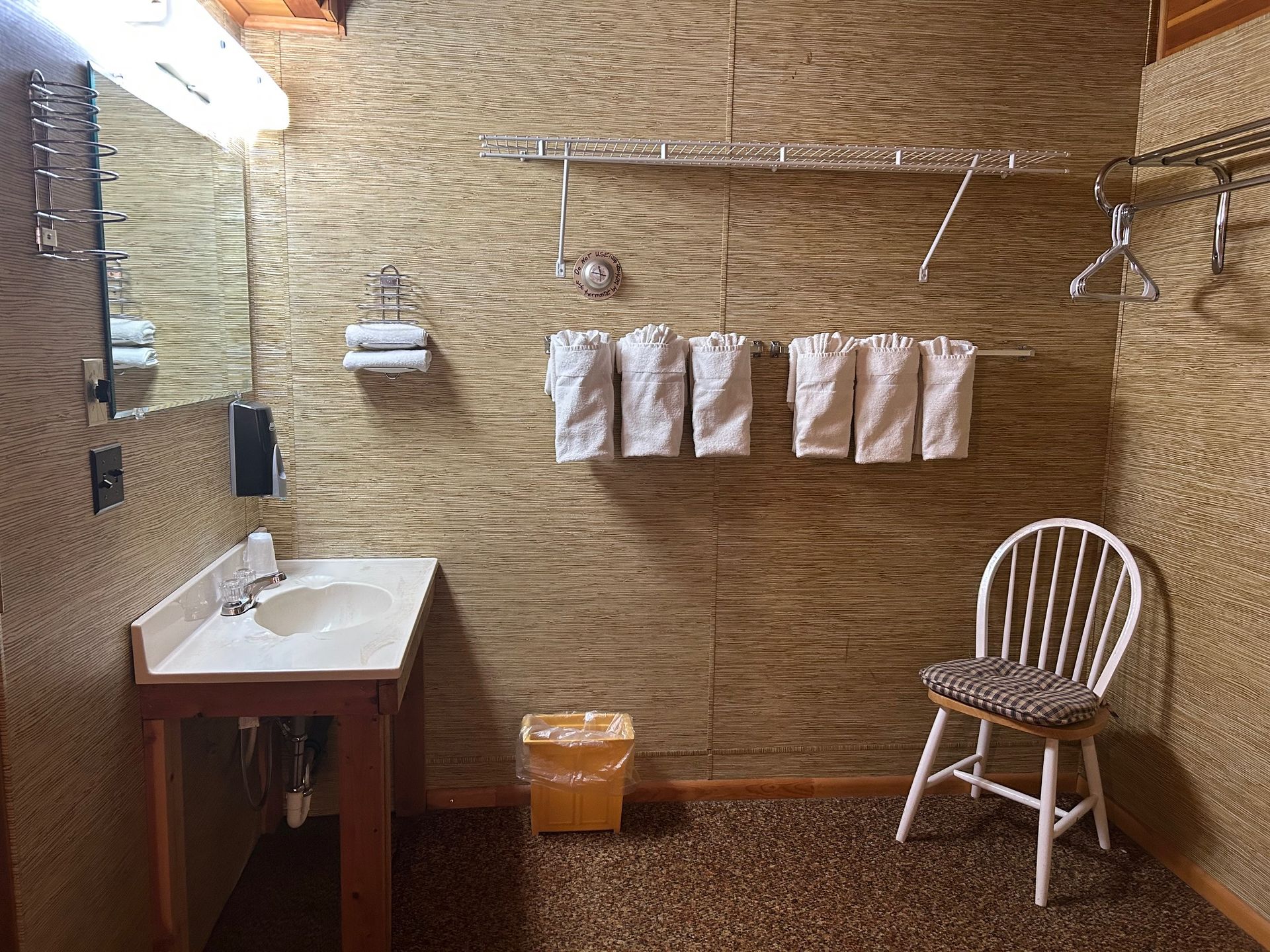 A bathroom with a sink , chair , mirror and towels hanging on the wall.