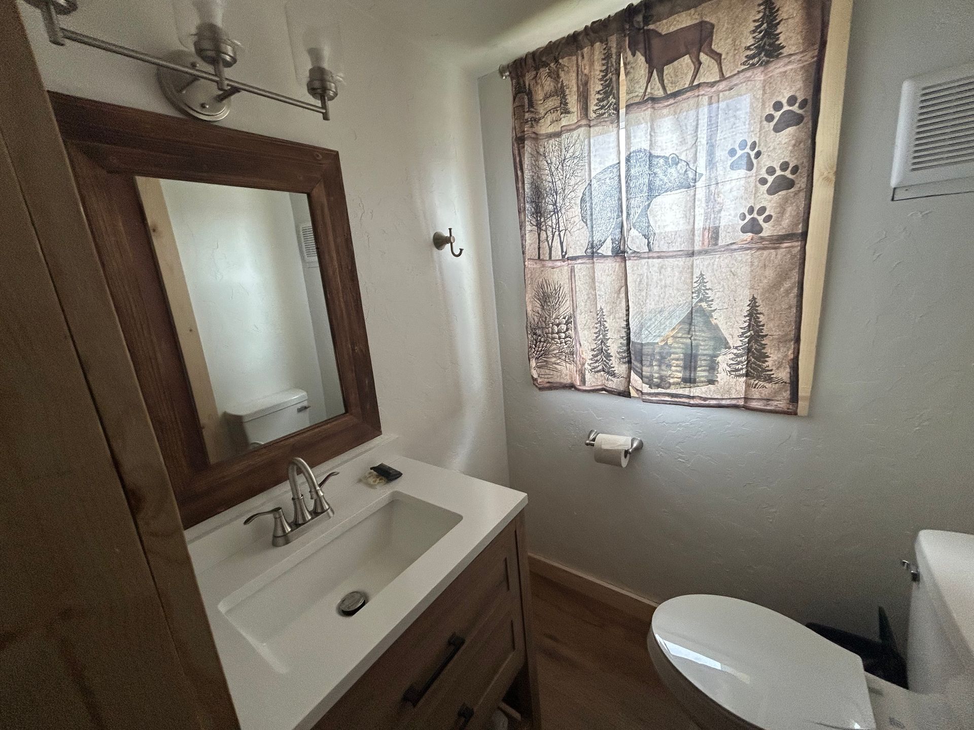 Bathroom with wooden vanity, mirror, and window with rustic curtains.