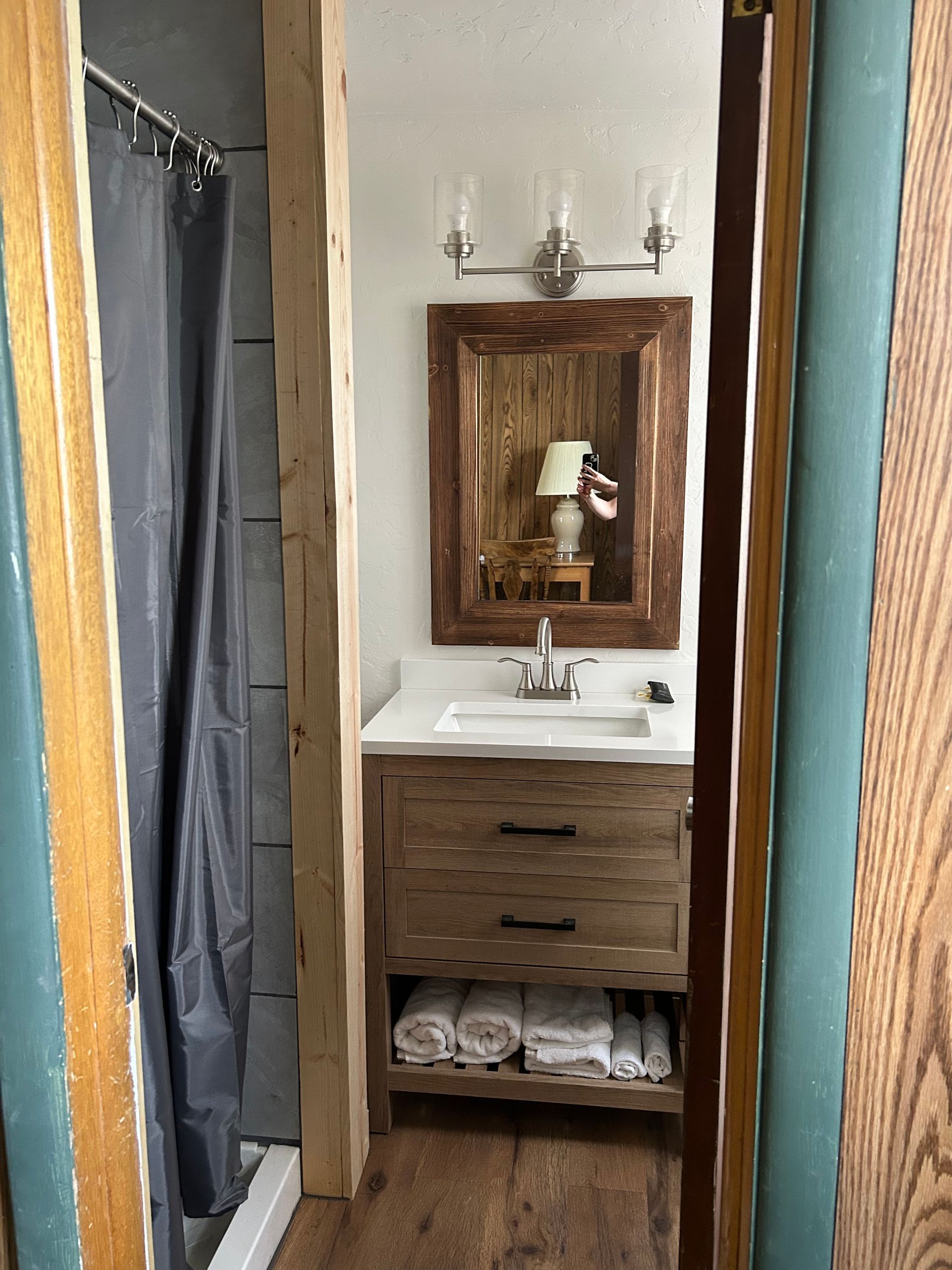 Bathroom with a wood vanity, framed mirror, and a shower curtain visible through the doorway.