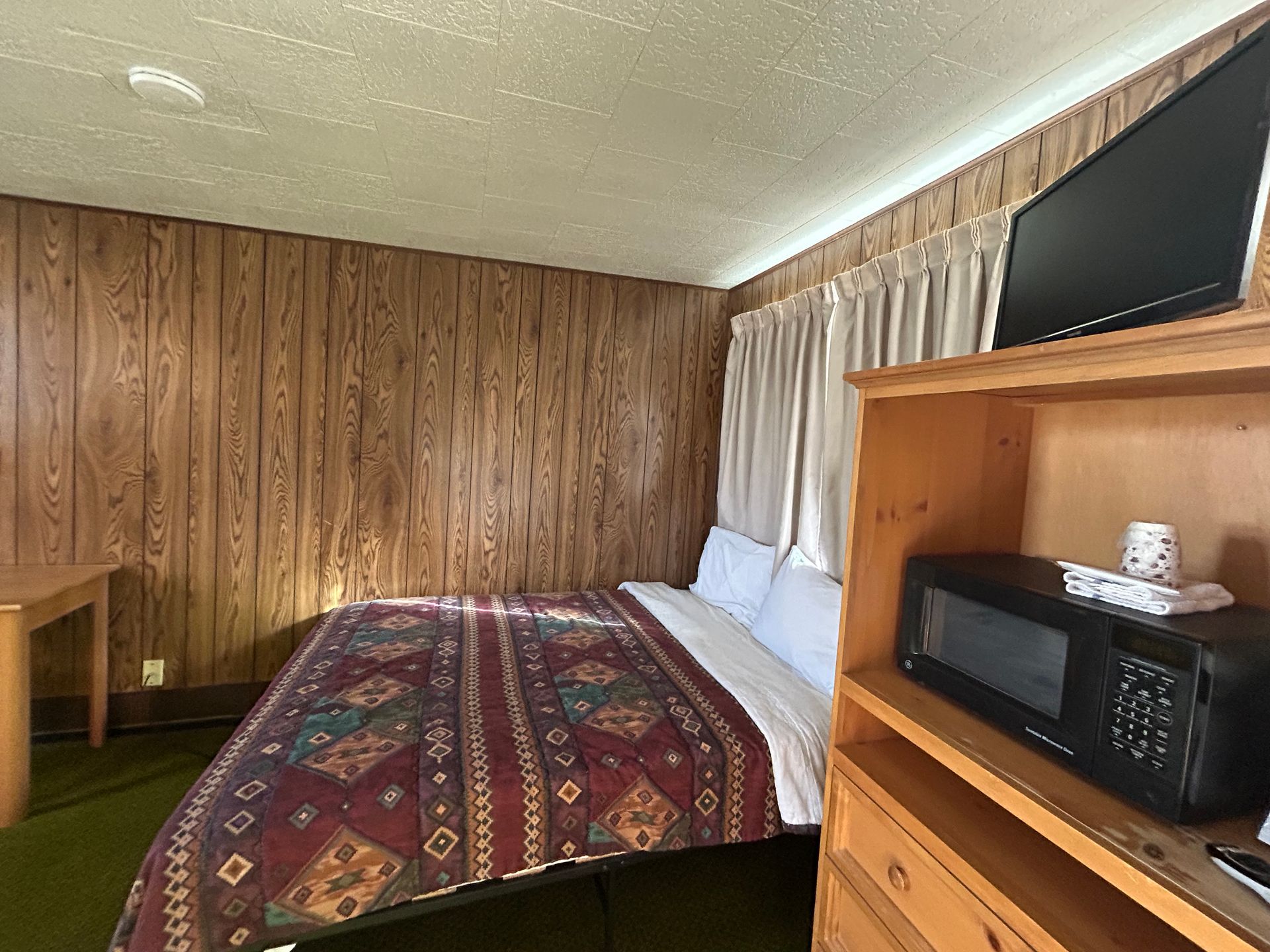 A motel room with wood paneling, a bed, microwave, TV, and a small desk.