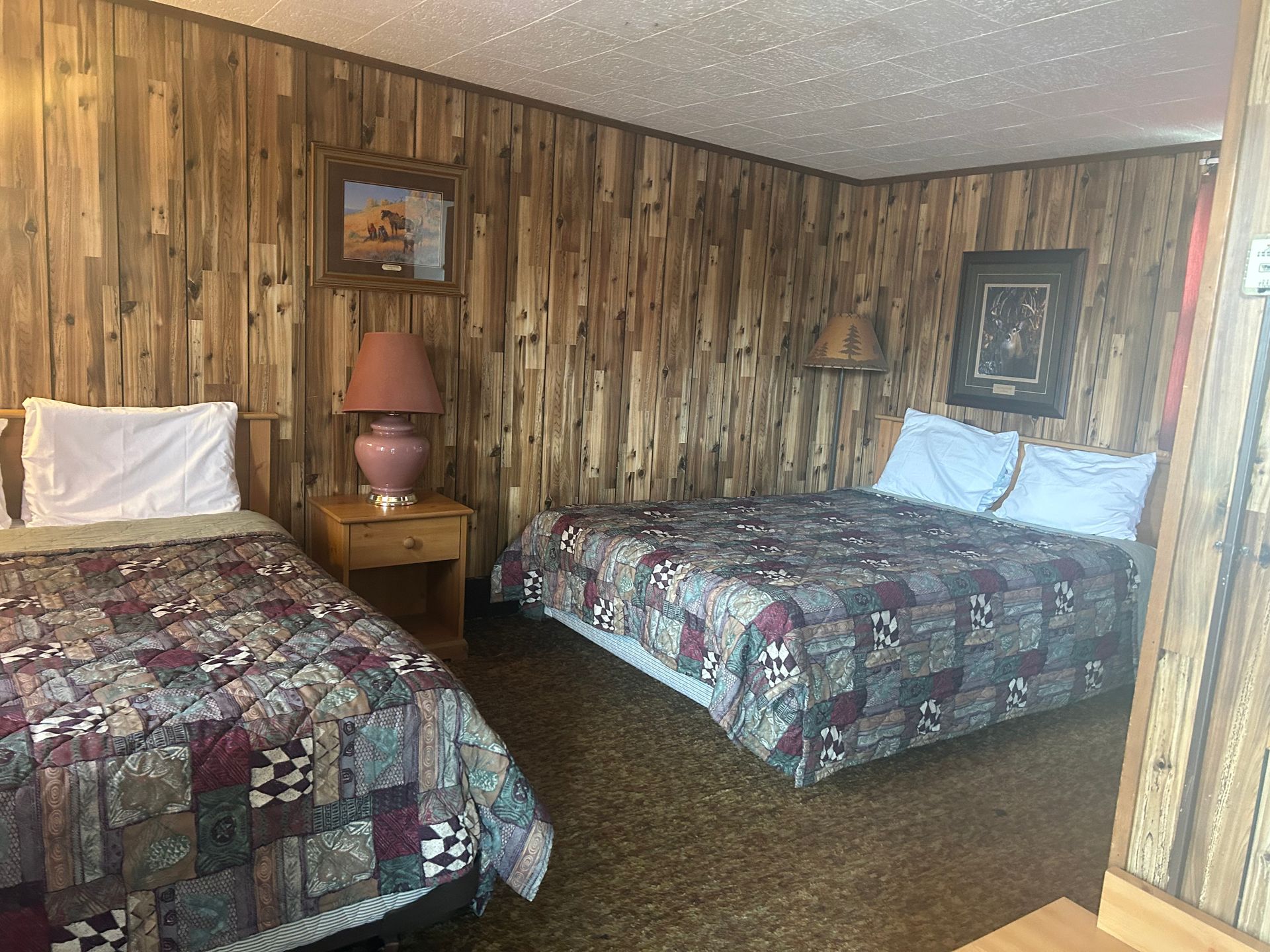 Motel room with two beds, wood panel walls, and framed artwork.