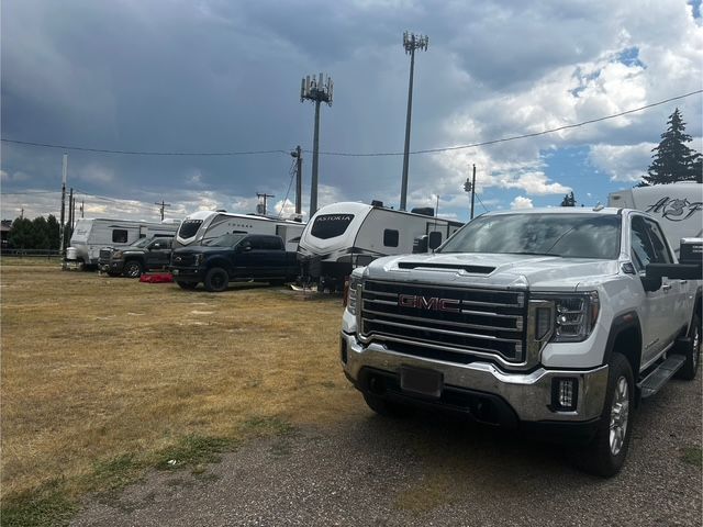 White GMC truck parked in front of RVs on a dry, grassy lot under a cloudy sky.