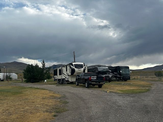 RVs and trucks parked on a gravel lot under a cloudy sky in a rural area.