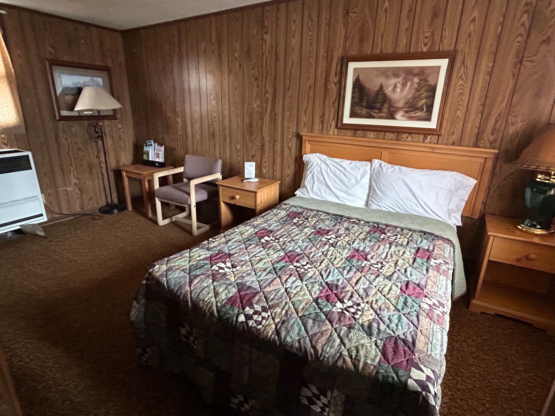 A hotel room with a bed , chair , nightstand , desk and lamp.