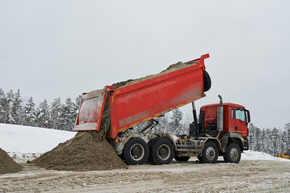 Un camion rosso sta scaricando terra in un campo innevato.