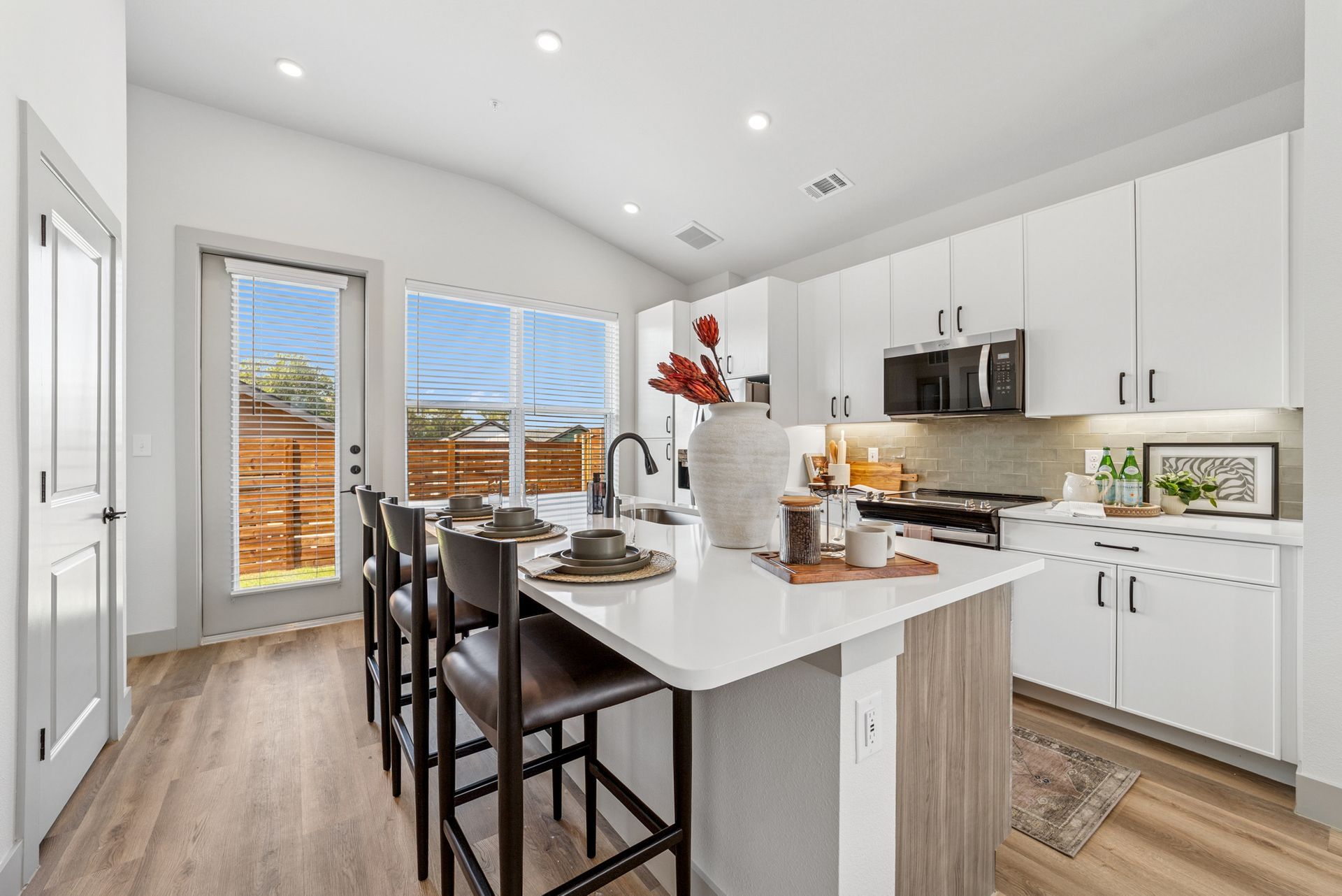 Modern kitchen with white cabinets, island with stools, and large windows.