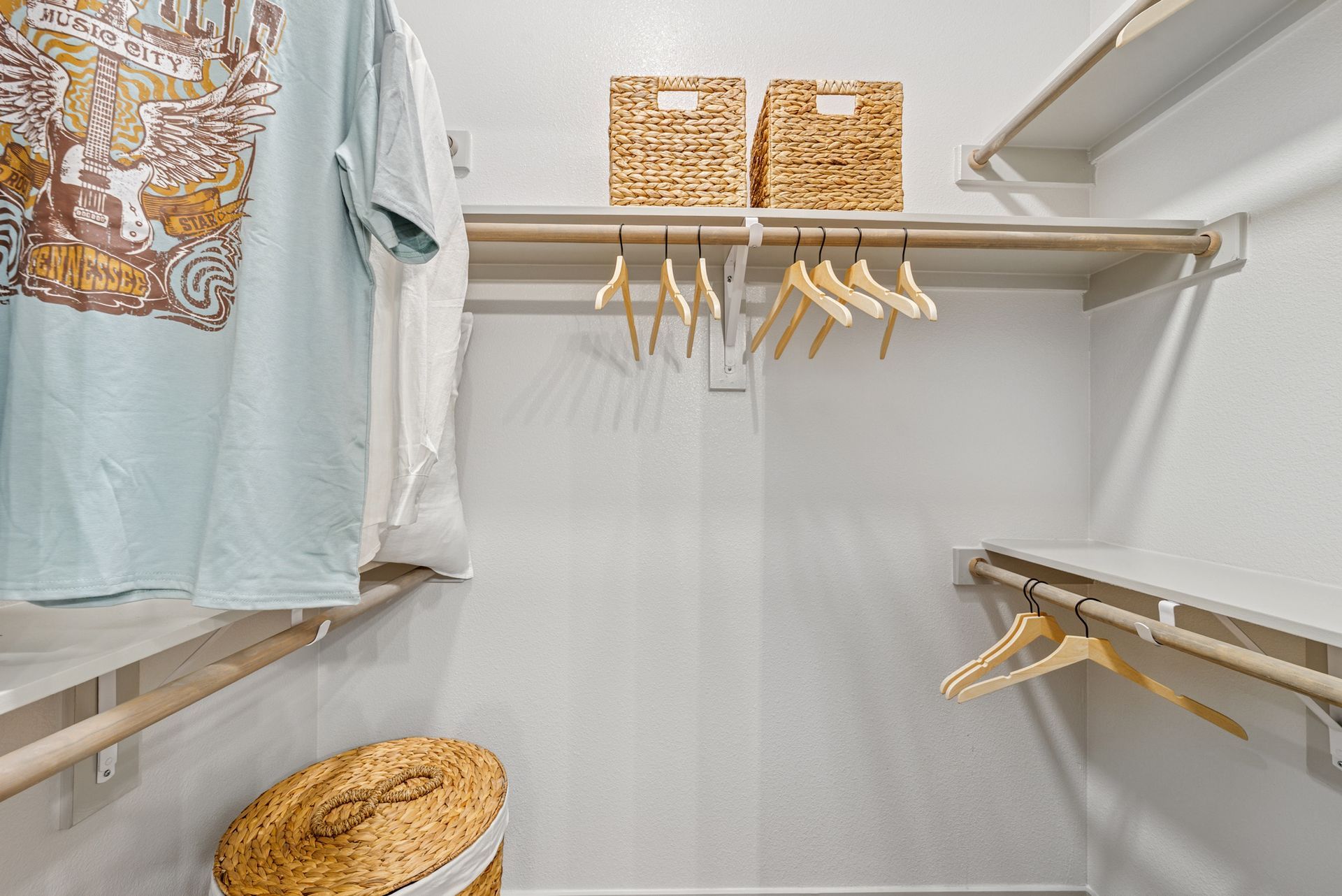Empty white closet with hanging rod, shelves, woven baskets, and clothes.