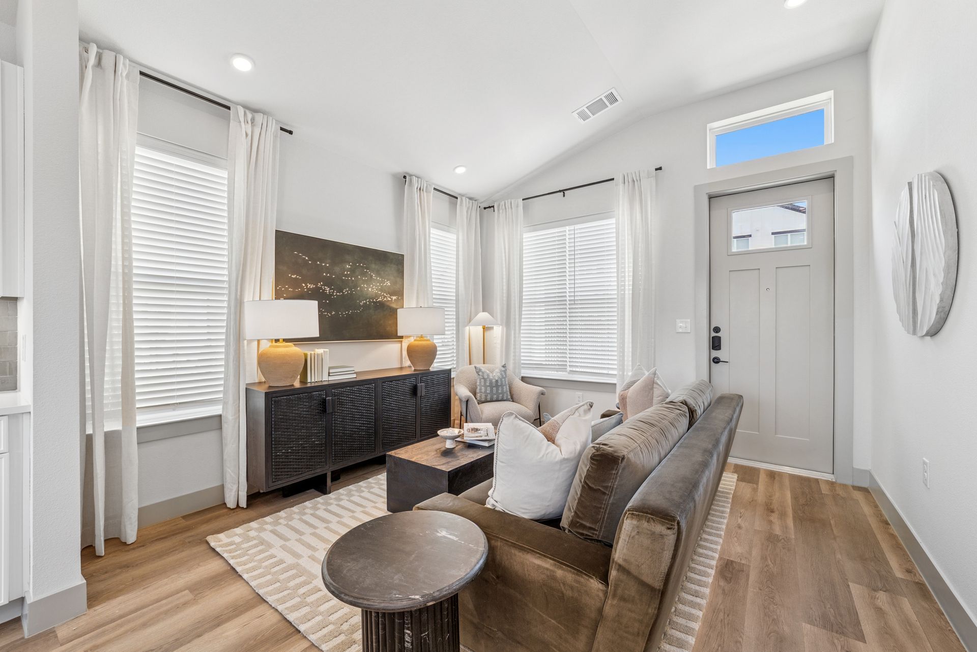 Living room with neutral tones, hardwood floors, sofa, TV, and large windows.