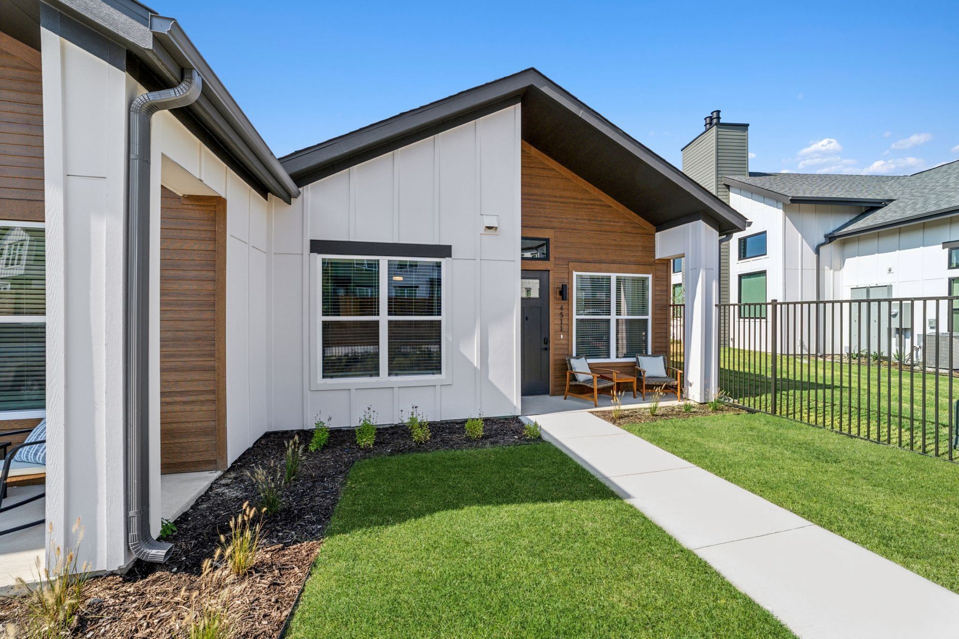 Modern white and wood-paneled house with a walkway, green lawn, and blue sky.