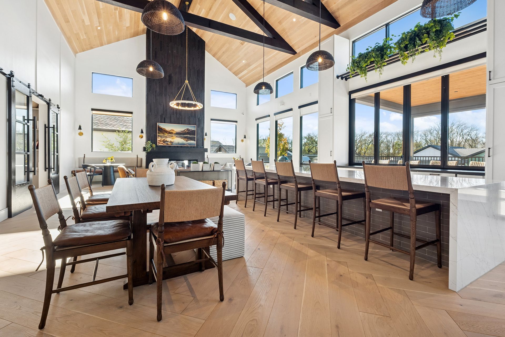 Spacious, modern room with high ceilings, dining table, bar seating, large windows, and decorative lighting.
