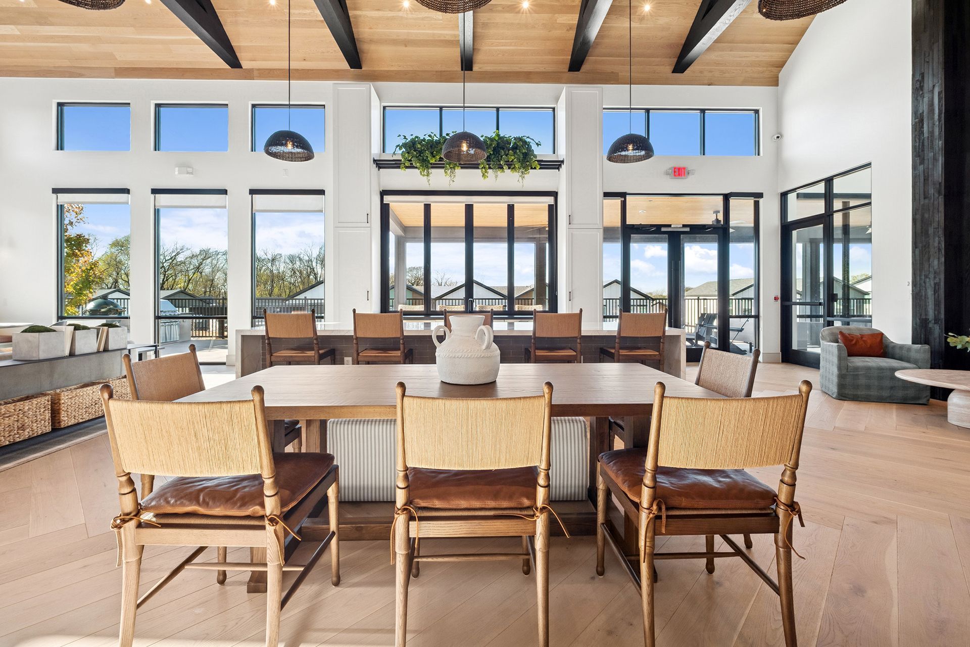 Large, light-filled room with long wooden table and chairs, large windows, and decorative plants.