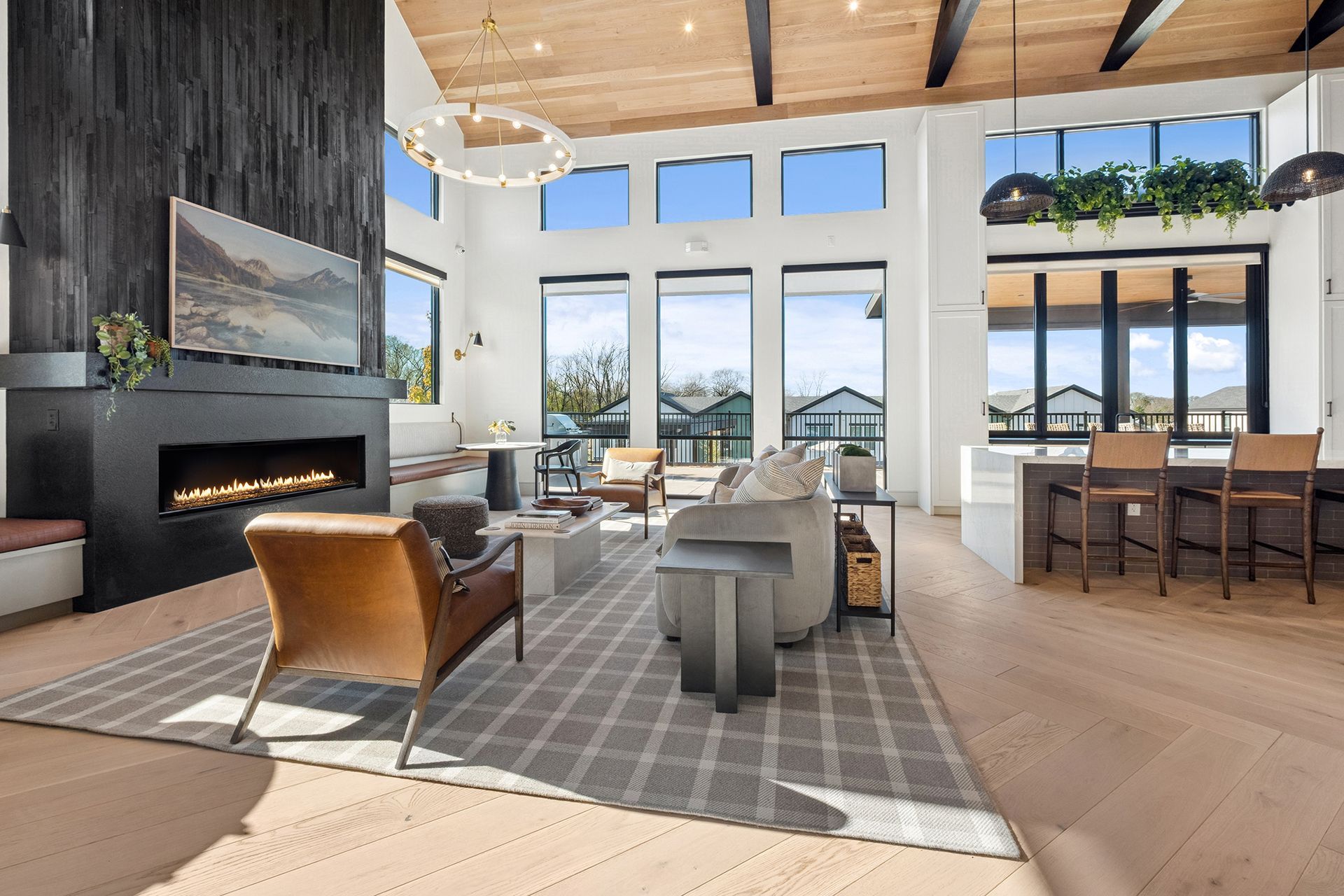 Modern living room with fireplace, large windows, light wood floors, and open kitchen.