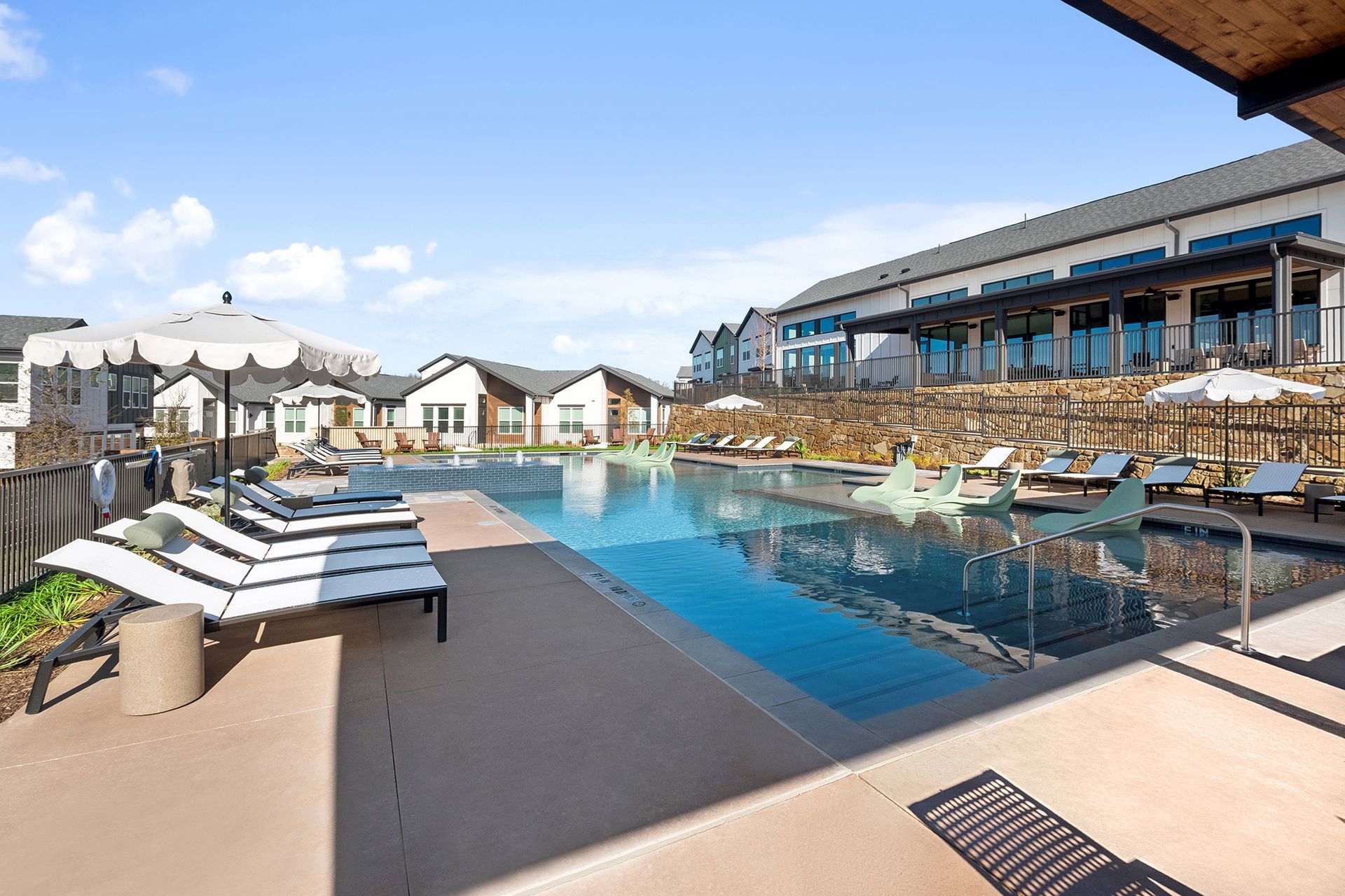 Swimming pool with lounge chairs, umbrellas, and building in the background on a sunny day.