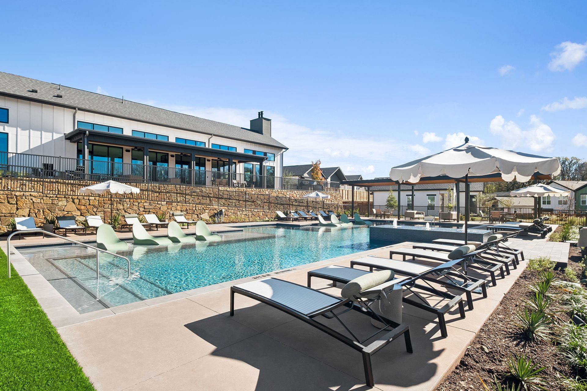 Pool area with lounge chairs, umbrella, and a building on a sunny day.