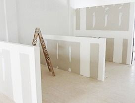 Interior de una habitación en construcción con paneles de yeso y una escalera de madera.