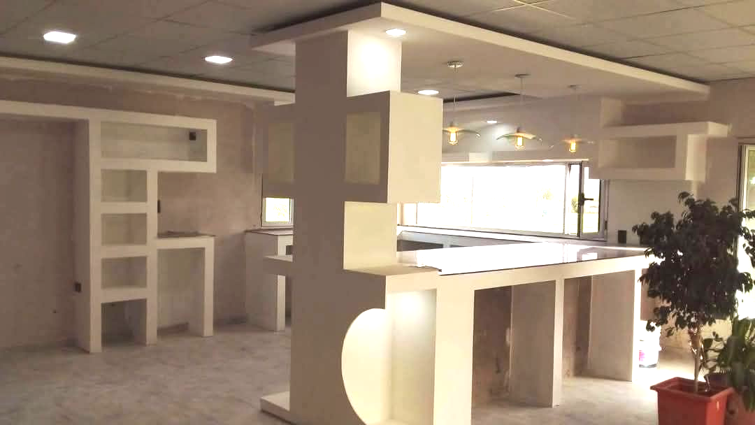 Interior moderno y minimalista con estructuras blancas, incluyendo un pilar con recortes cuadrados y una larga barra.