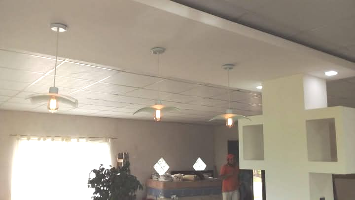 Vista interior: lámparas colgantes, techo texturizado, una persona vestida de naranja y estantes empotrados en la pared.