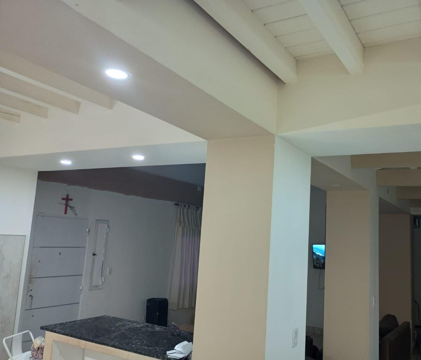 Vista interior de una habitación con paredes blancas, luces empotradas y vigas de madera a la vista.